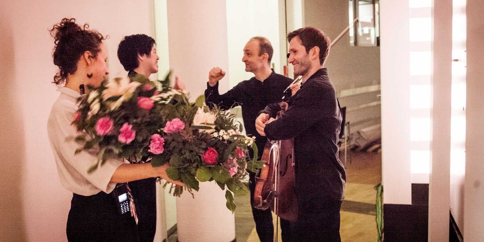 Four people are happily chatting backstage, one person is holding a bouquet of flowers.