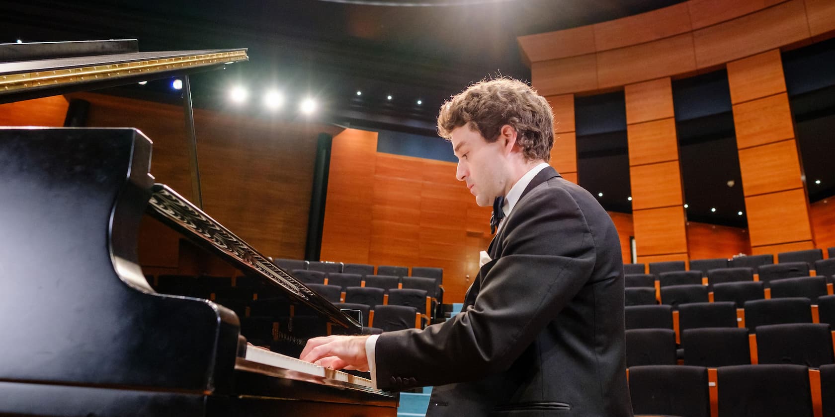 Man in a suit playing the piano in an empty concert hall.