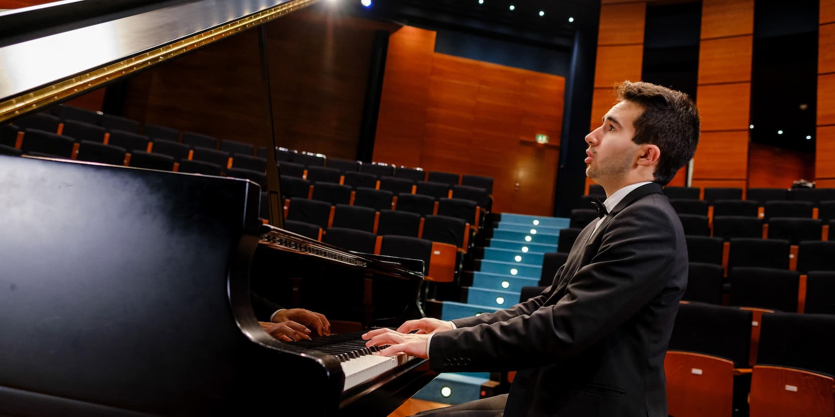 A man playing piano in an empty concert hall.