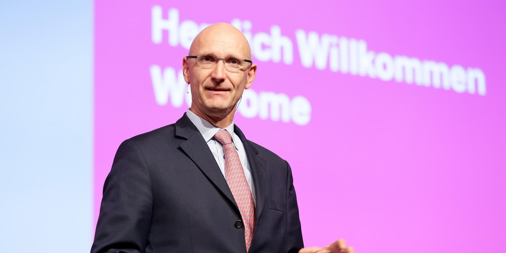 Man standing on a stage in front of a screen with the text 'Welcome'.