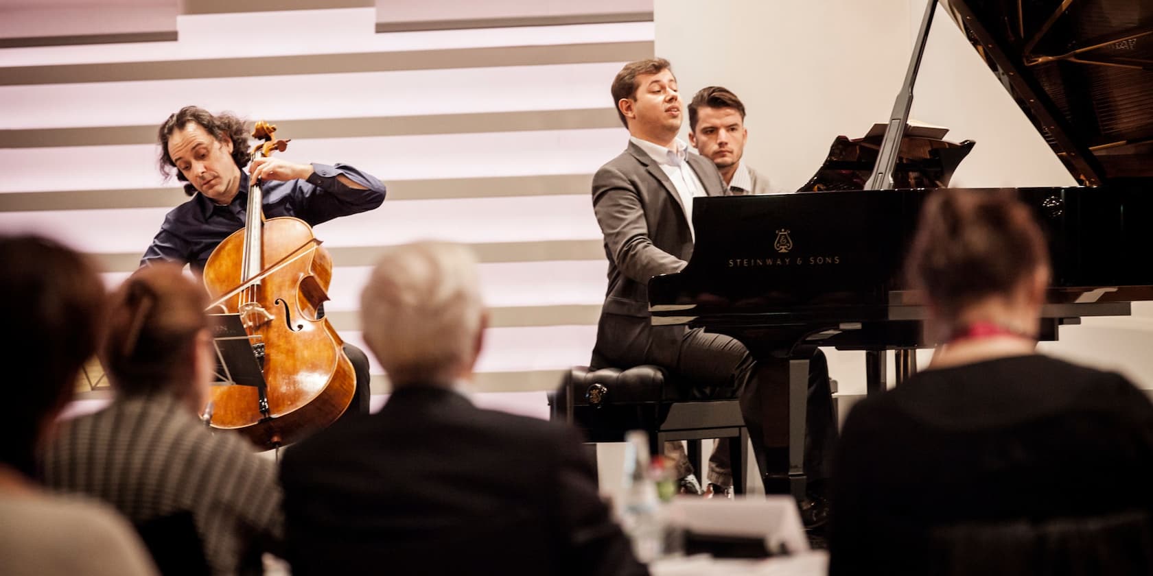 A cellist and a pianist perform in front of an audience.