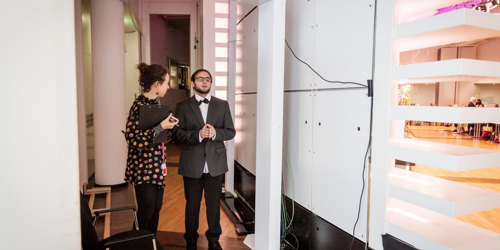 A woman and a man in formal attire standing next to a white room divider.