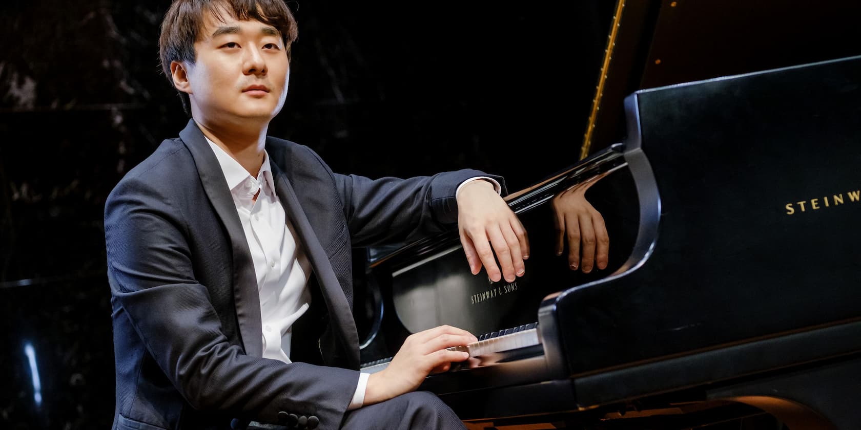 Man in a suit playing a Steinway & Sons grand piano.