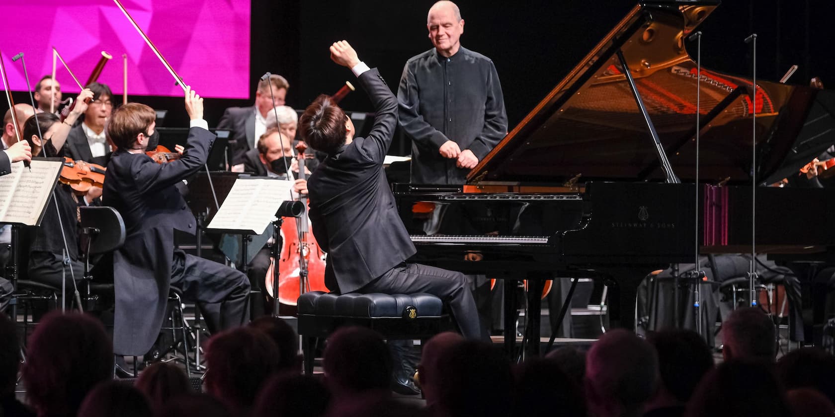 A pianist and a conductor perform with an orchestra.