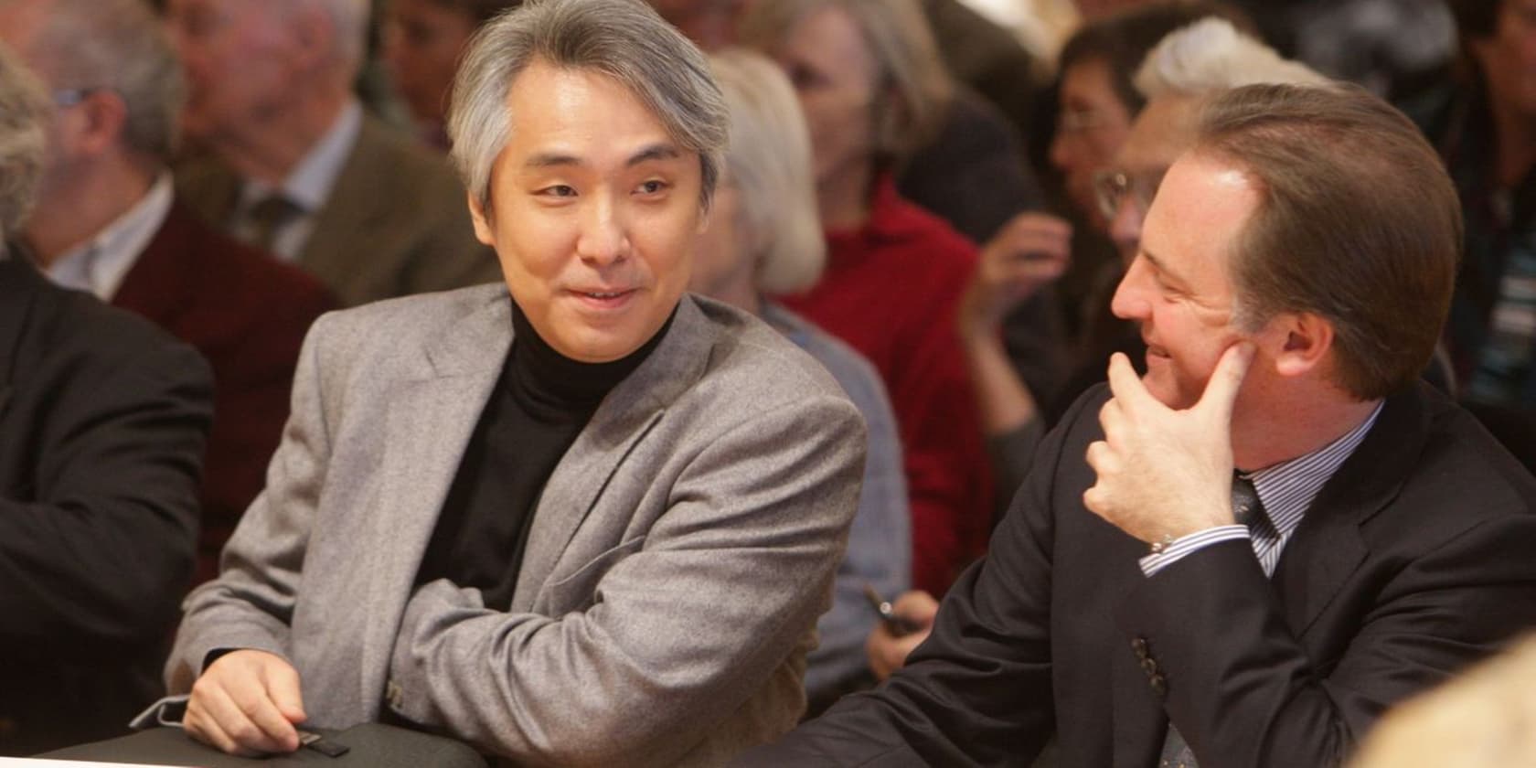 Two men sitting next to each other and conversing at an event.