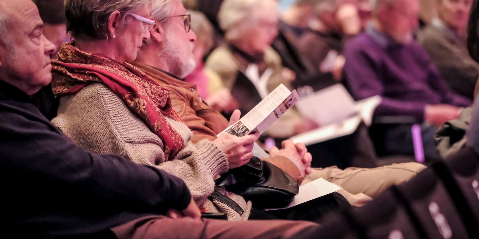 A group of elderly people sitting and reading brochures at an event.