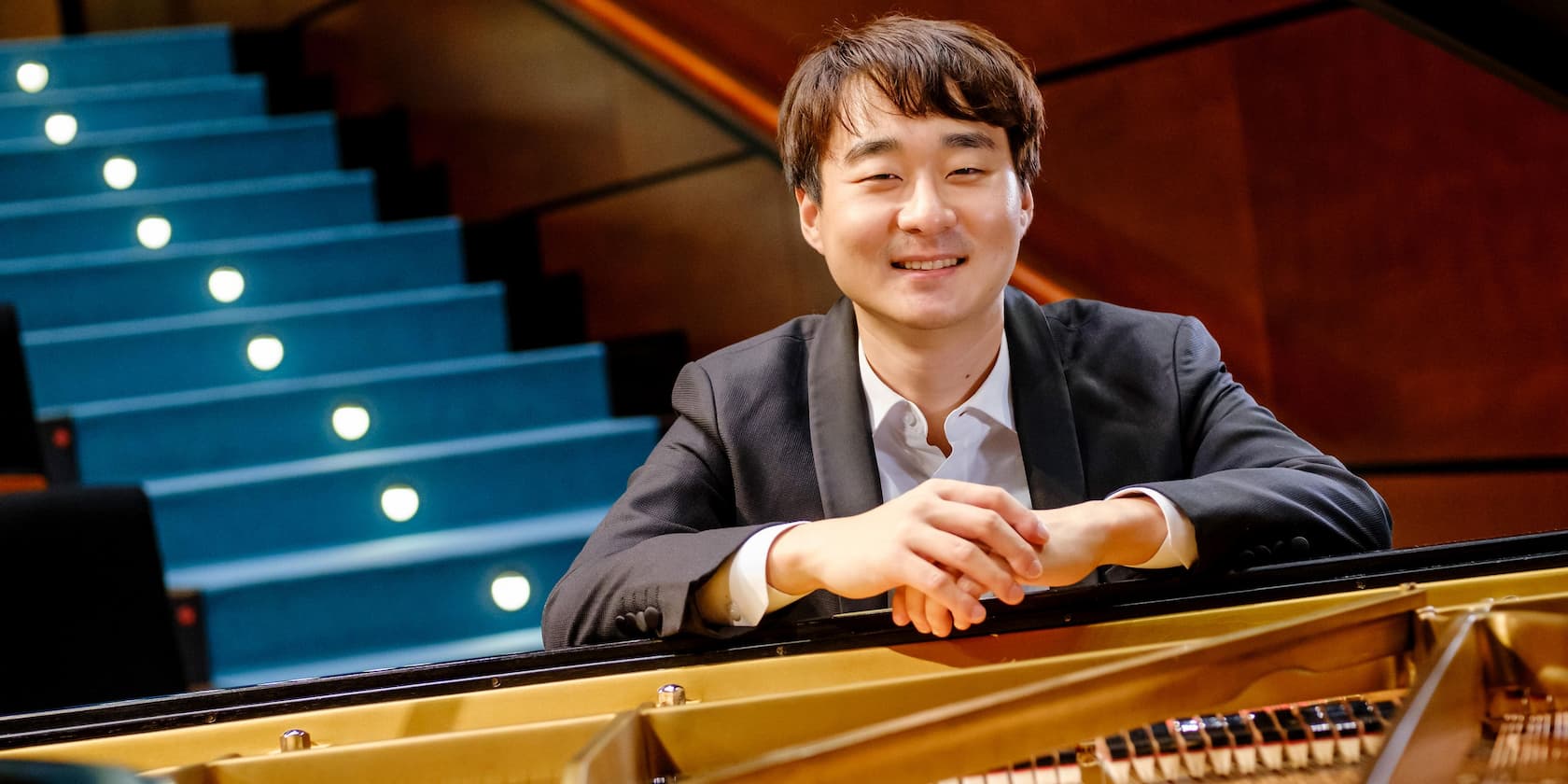 A man smiles while sitting behind a grand piano.