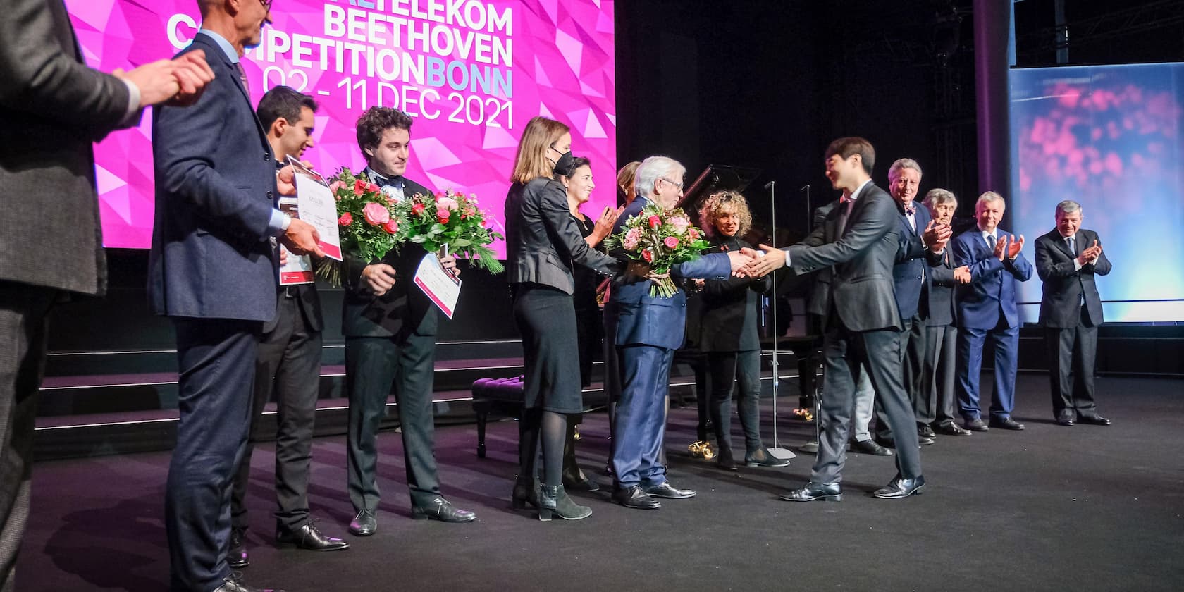 Award ceremony at the Telekom Beethoven Competition Bonn in December 2021. People are standing on a stage handing over bouquets of flowers and certificates.