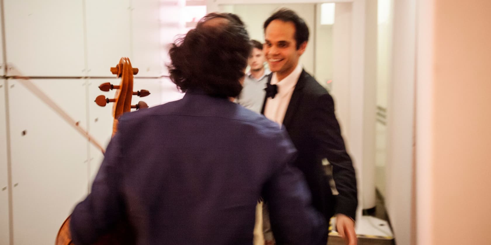 A person in a suit greets a cellist.