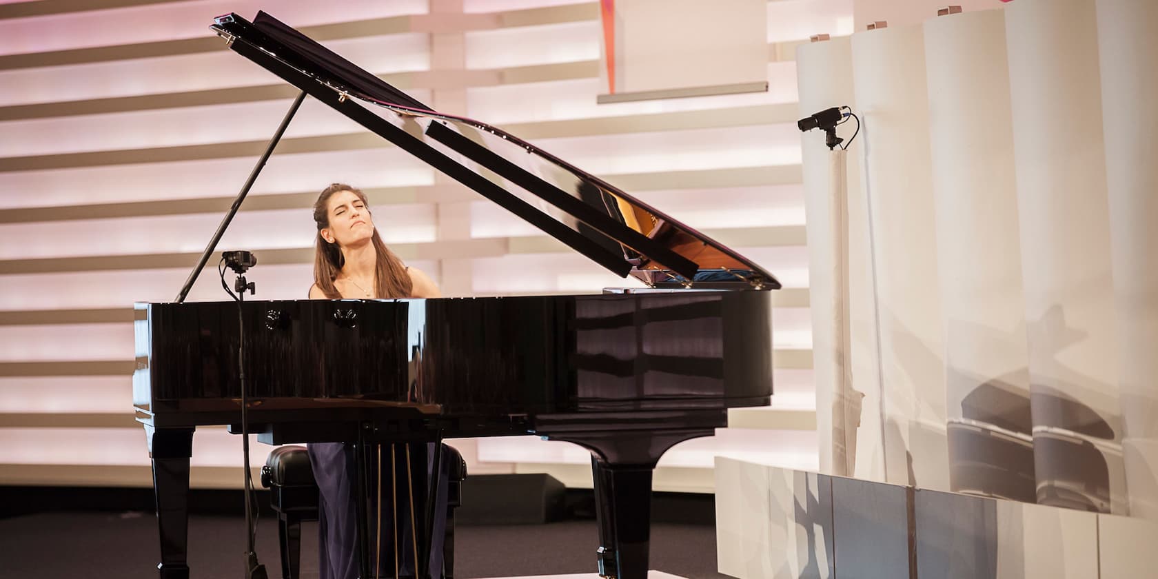 A woman plays a black grand piano in a modern room