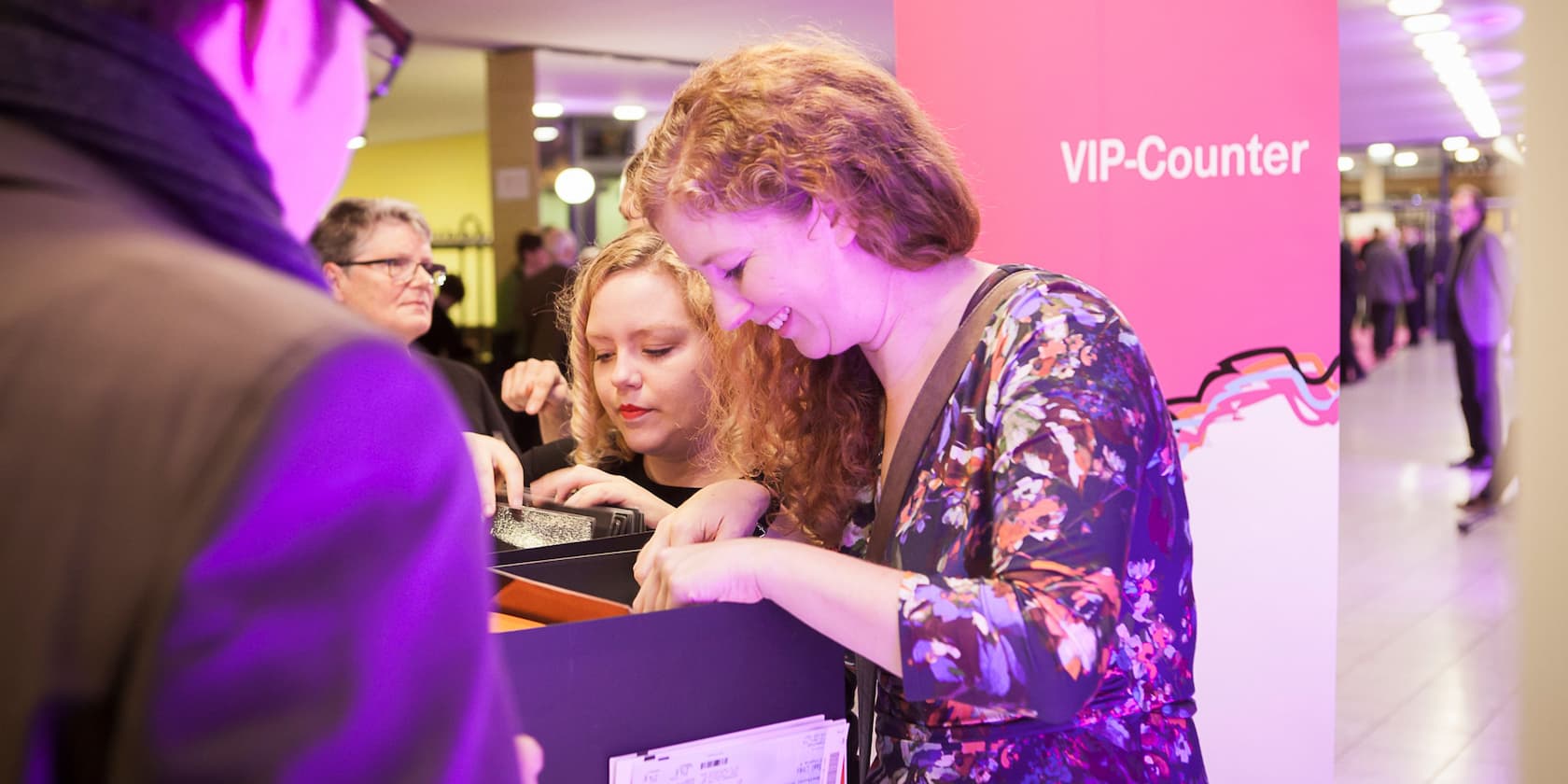 Zwei Frauen lächeln und durchsuchen eine Kiste am VIP-Counter.