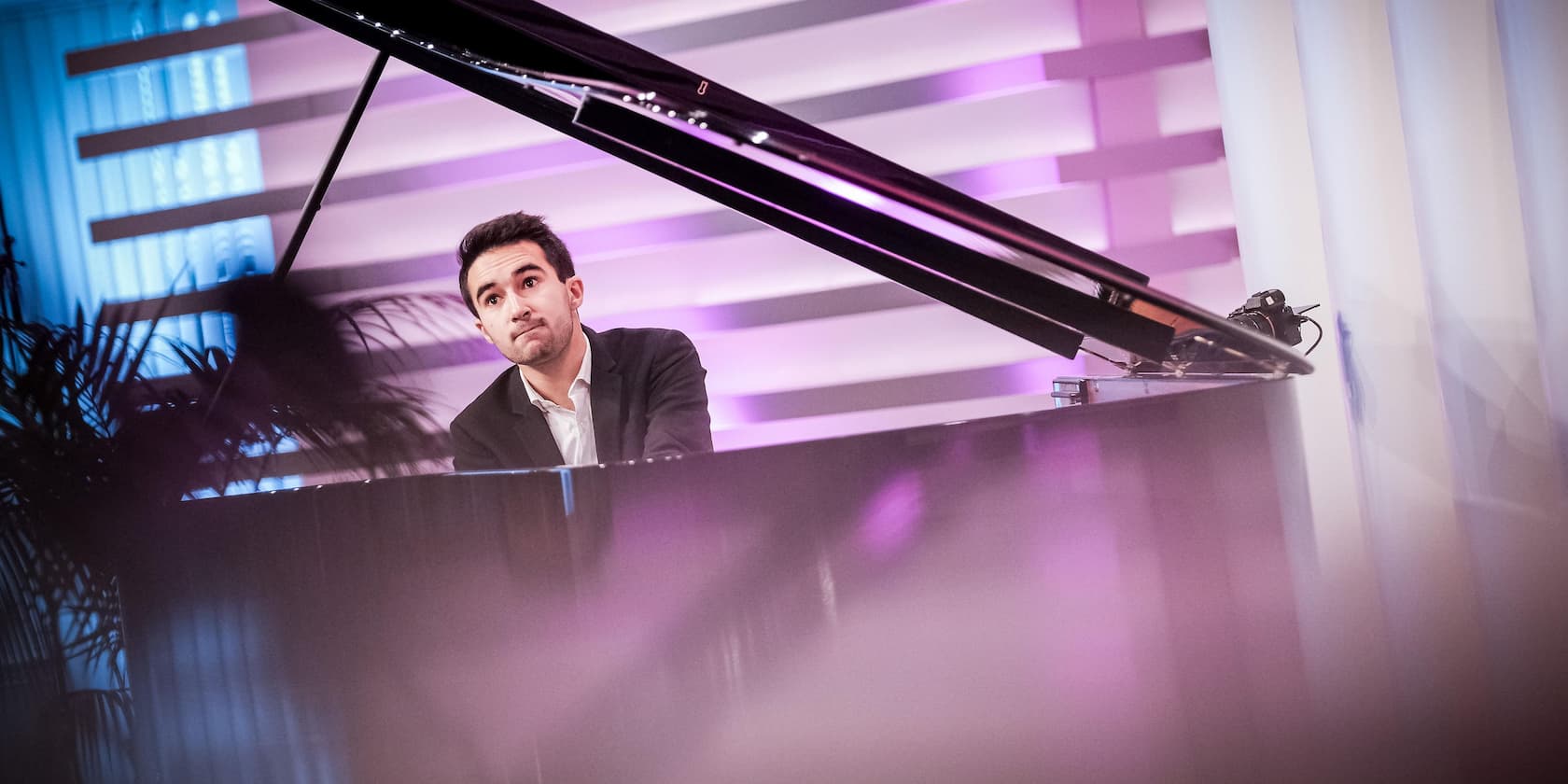 A man playing the piano in a modern room with purple and blue lighting.