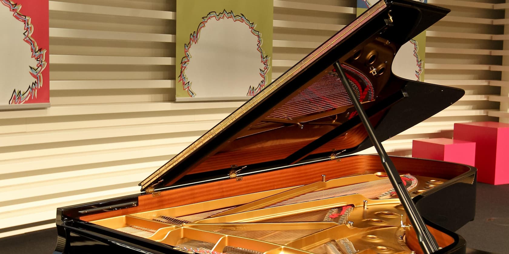 An open grand piano on a stage with colorful artworks in the background.