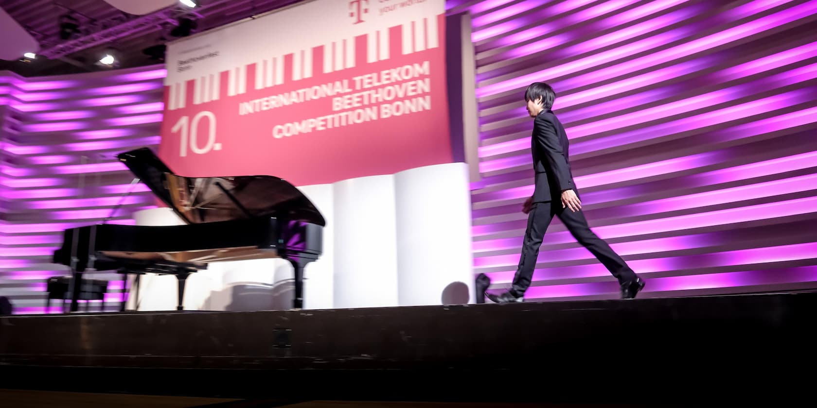 Man in a suit walks past a grand piano on the stage of the 10th International Telekom Beethoven Competition in Bonn.