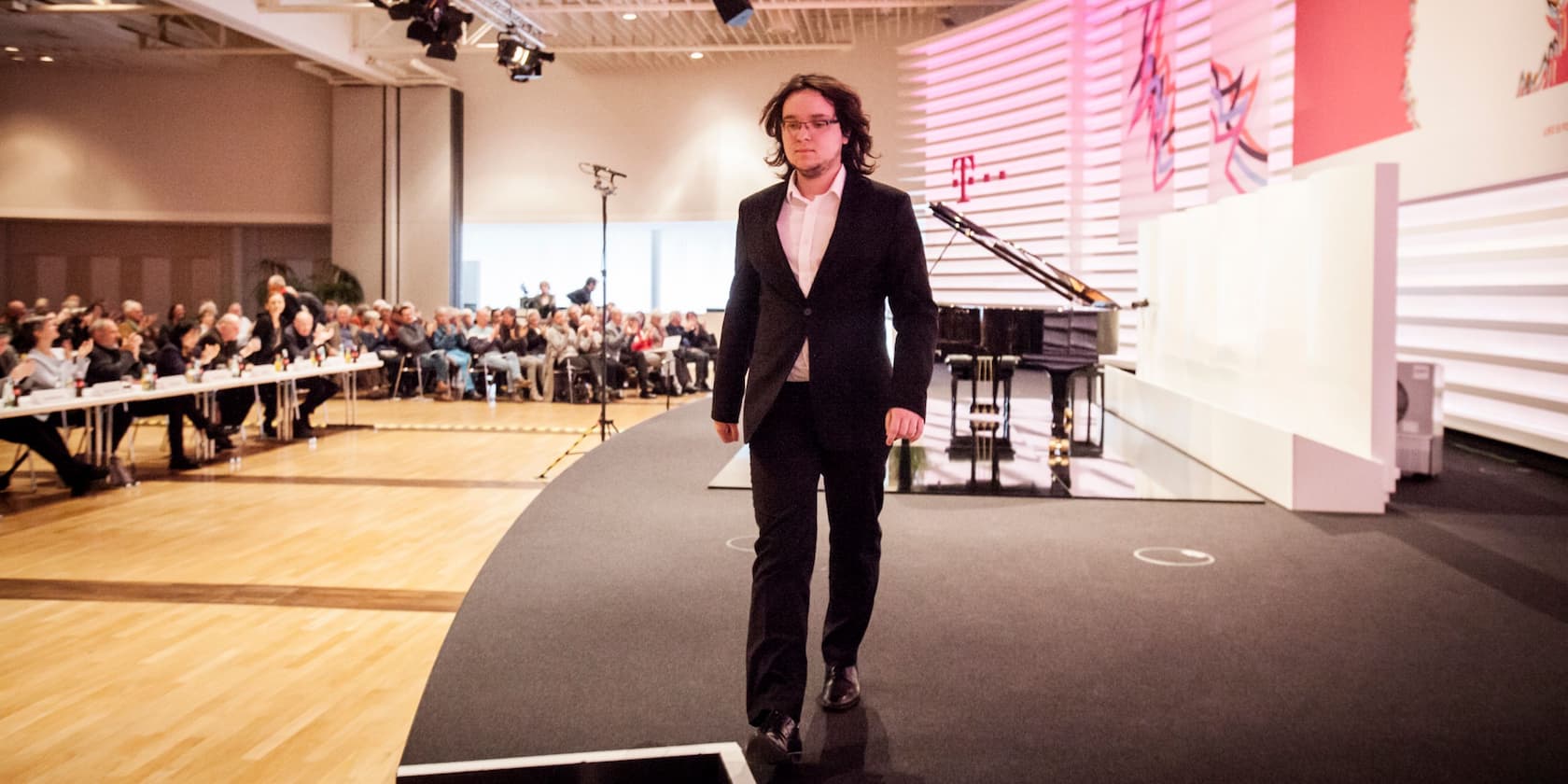 Man in a suit walking on a stage while the audience in the background applauds.