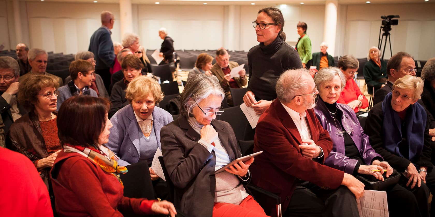 A group of elderly people gathered in a conference room, having conversations.