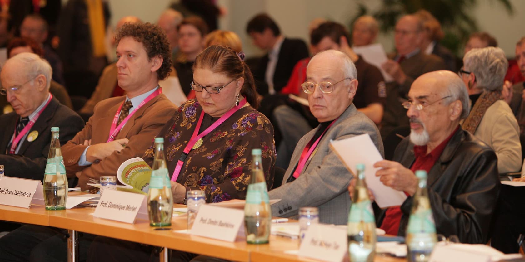 A group of people sitting at a table at a conference, reading documents.