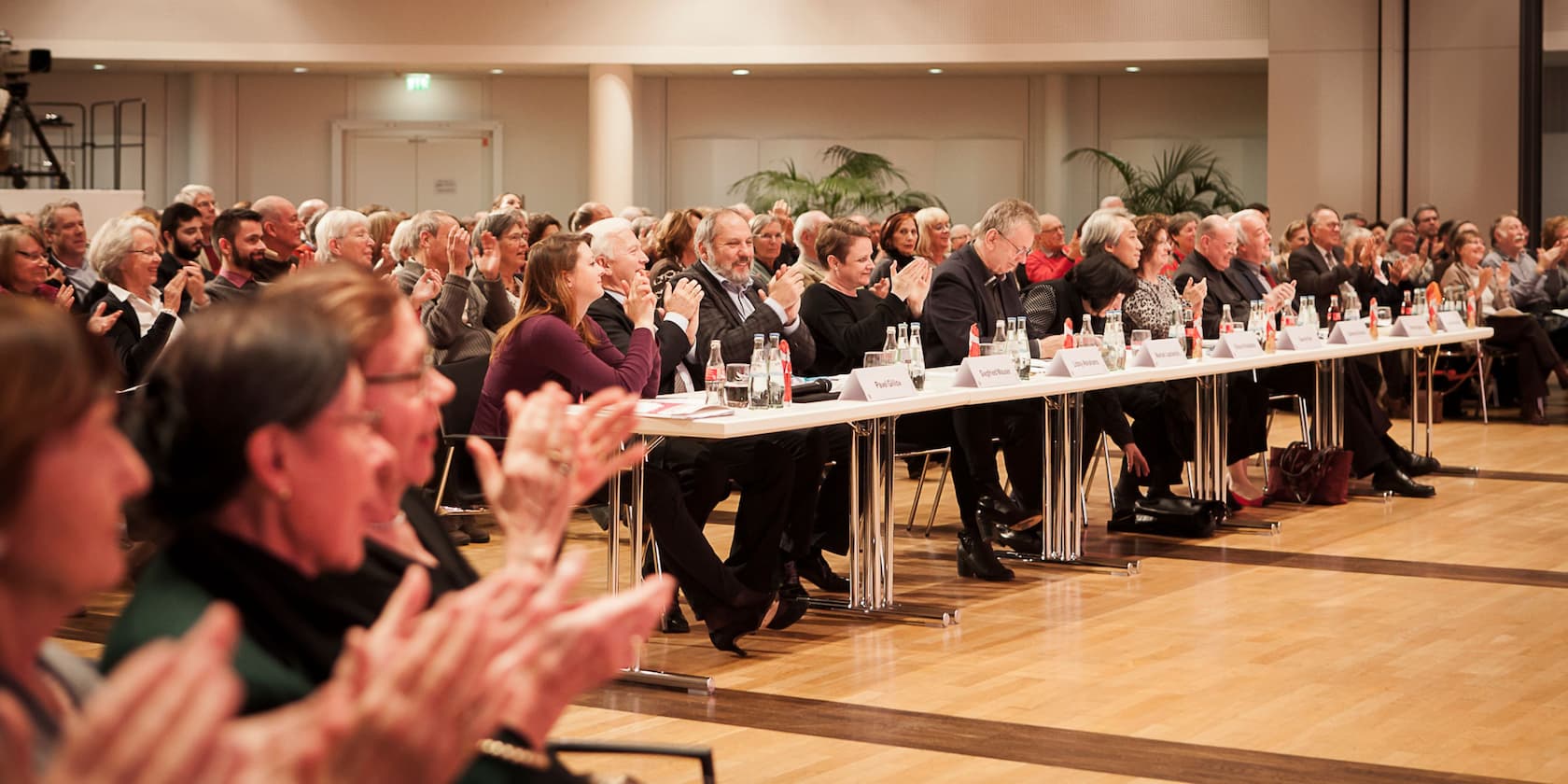 A group of people sitting at tables and clapping during an event.