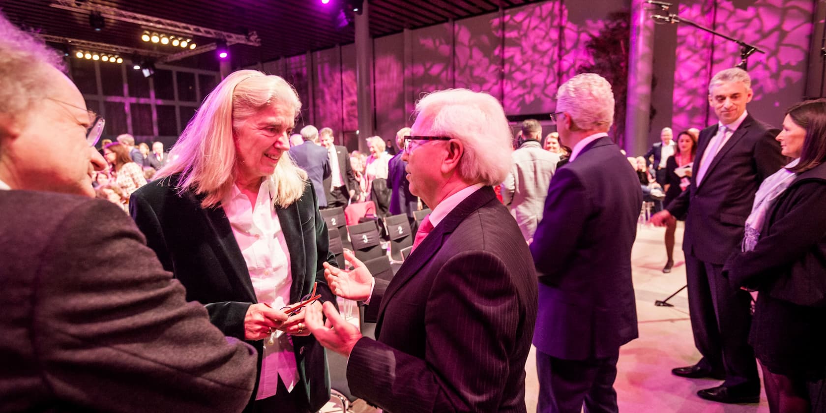 A group of people discussing at an event in a room with purple lighting.