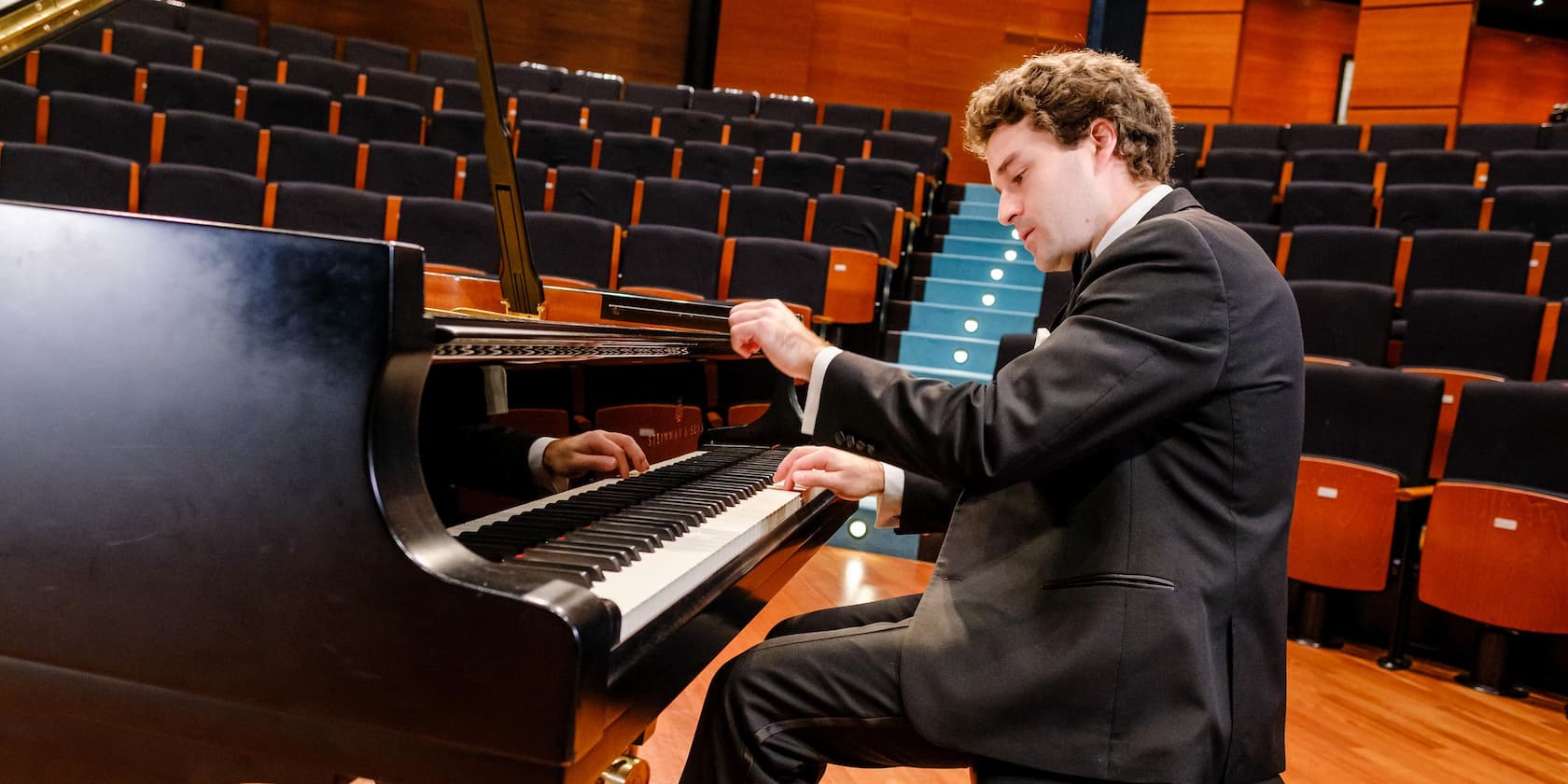 A pianist playing a grand piano in an empty concert hall.