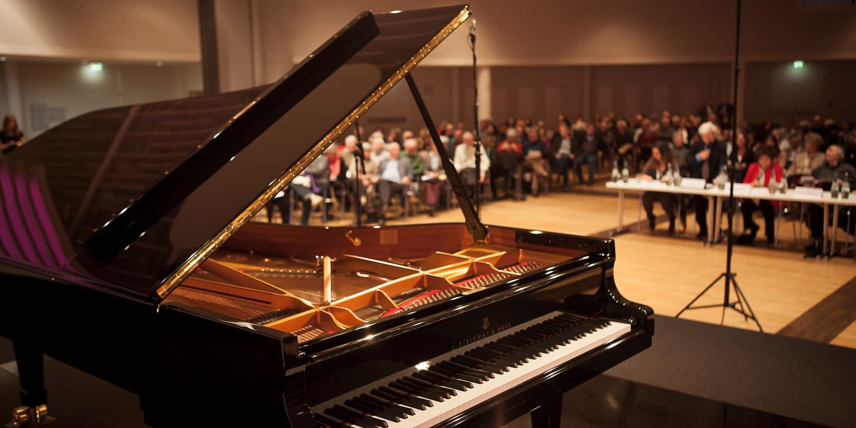 Grand piano on a stage in front of a seated audience.