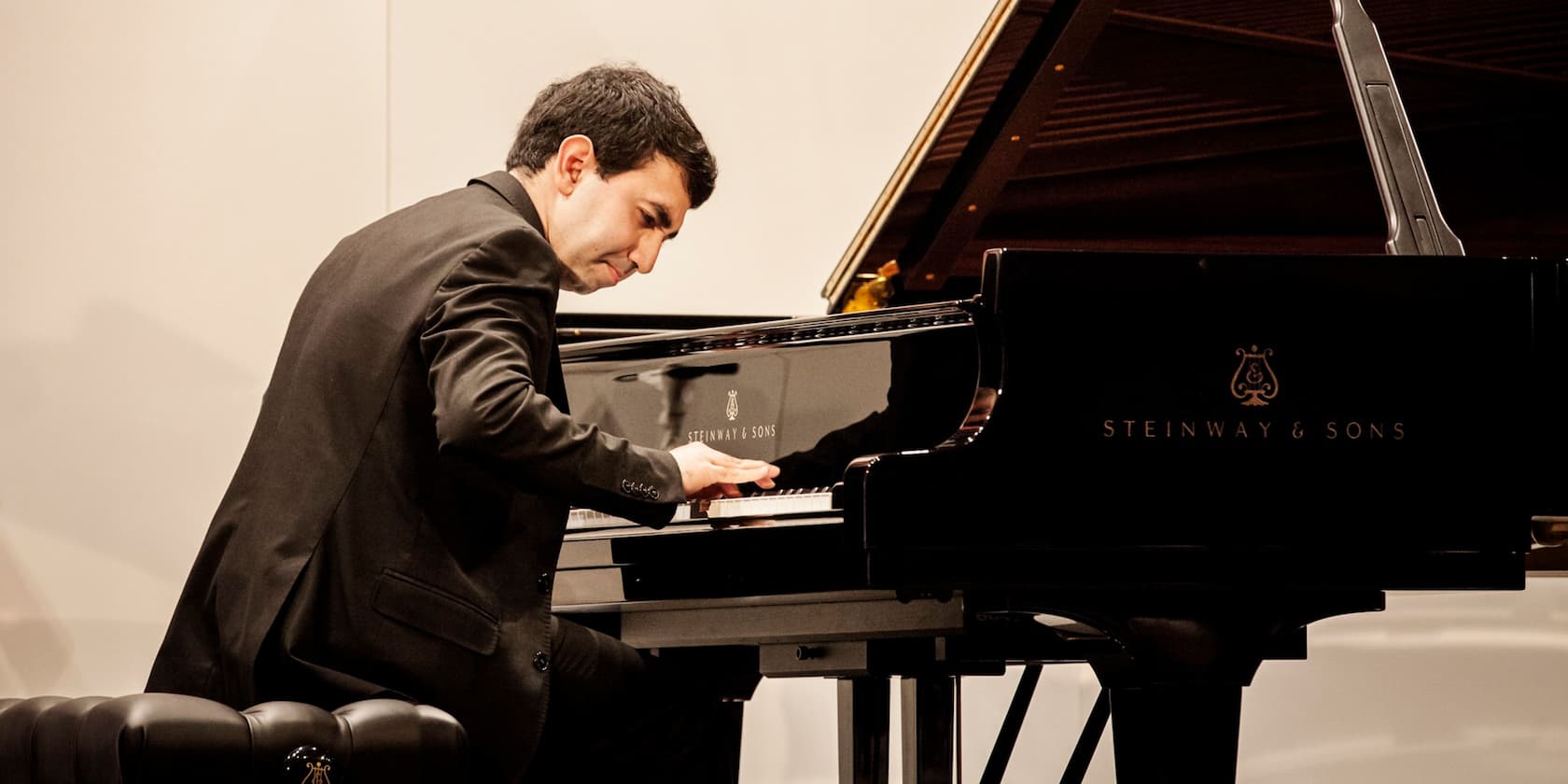 A man in a black suit playing a Steinway & Sons grand piano.