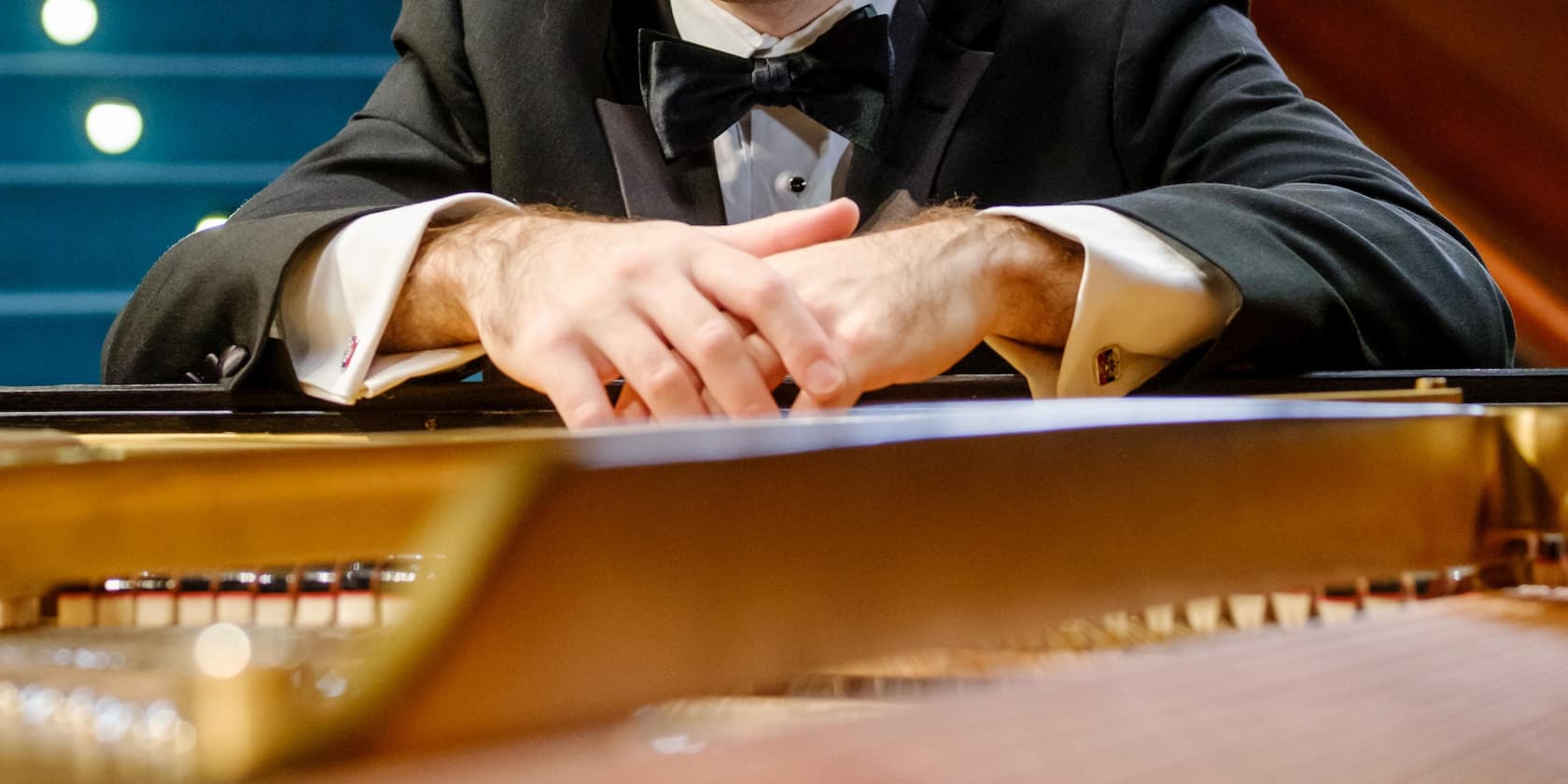 A pianist in a tuxedo sits at a grand piano.