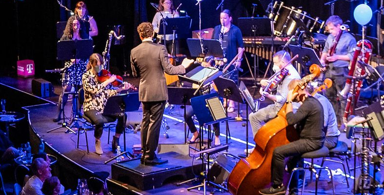 Großes Musikensemble spielt lebhaft auf der Bühne.