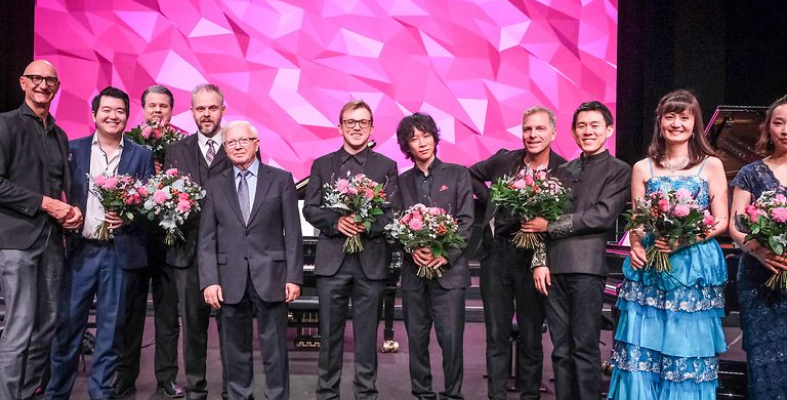 Winners and organizers of the Beethoven competition stand on stage holding bouquets.