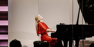 A woman with long, loose blonde hair plays the piano with her back straight and her head stretched backwards.