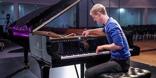 A blond man in a blue shirt works on the grand piano on stage.