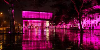 Through the darkness, a magenta-lit building with a glass façade can be seen.