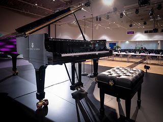 In the empty hall, the open grand piano and stool stand with a view of the still empty auditorium.